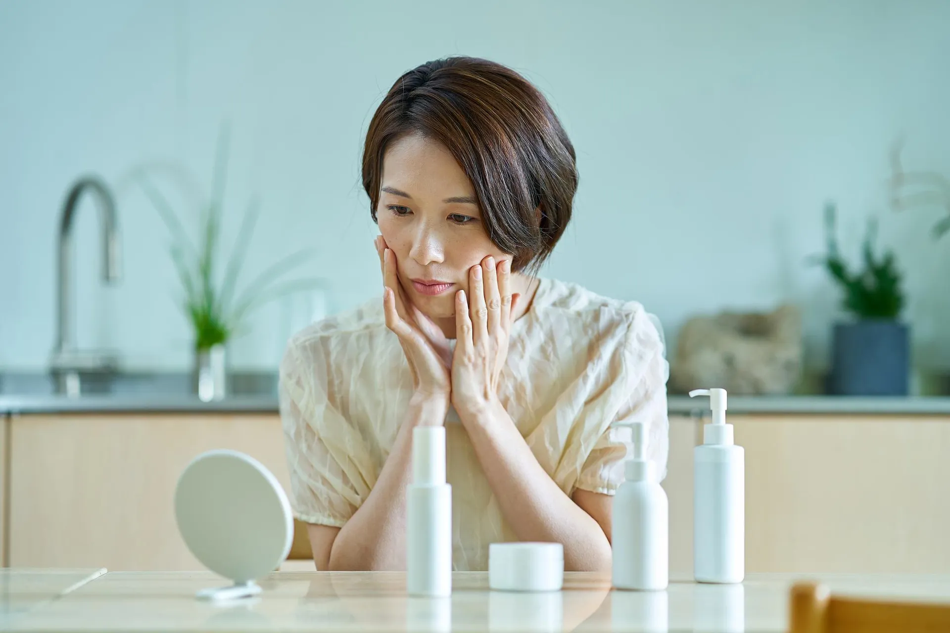 化粧品を並べて、自分の肌タイプを観察する中年女性のイメージ画像